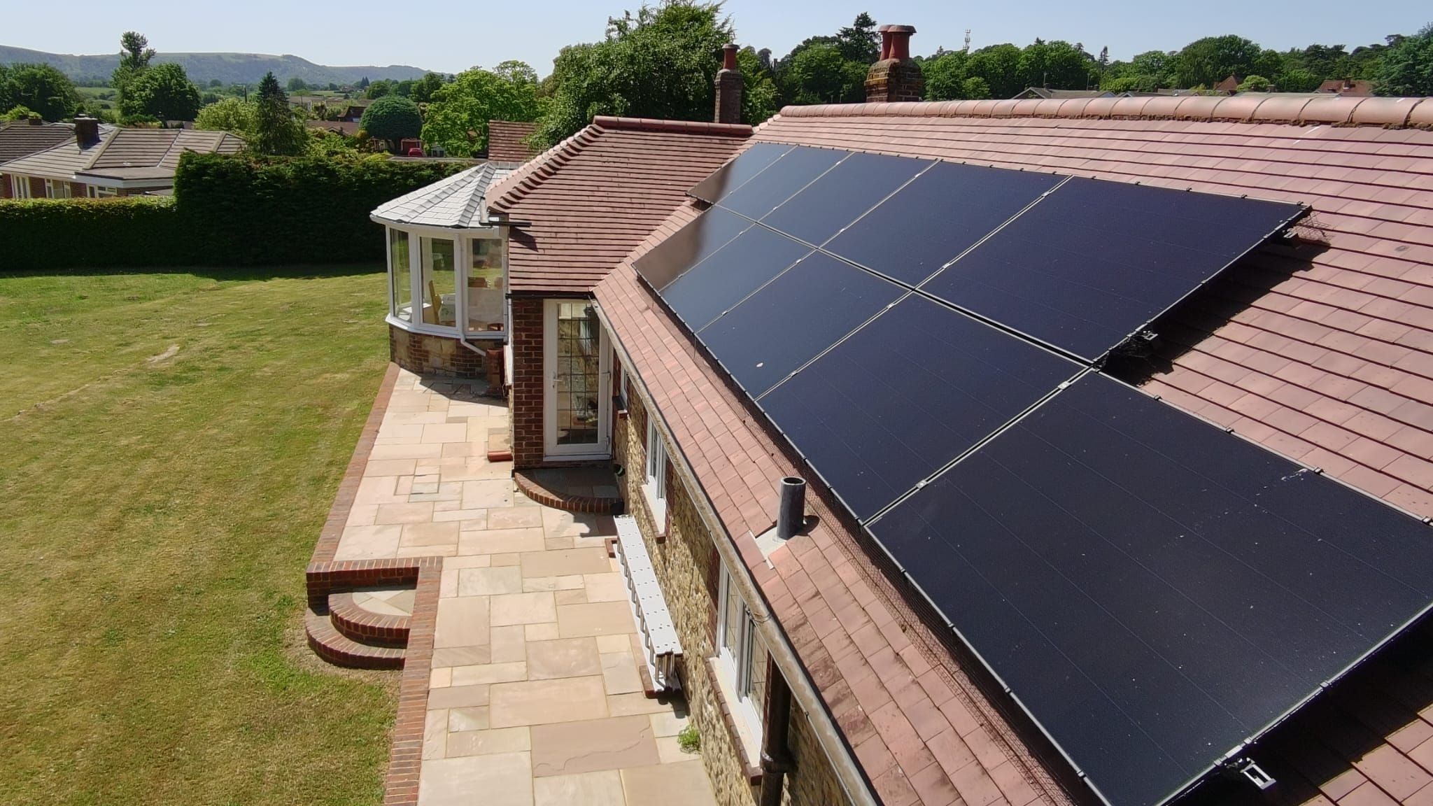 All-black solar panels on a clay-tiled bungalow roof, with hills on the horizon