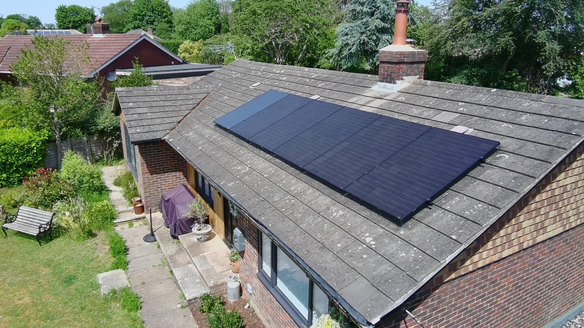 Aerial view of a bungalow with an all-black array, garden and patio below