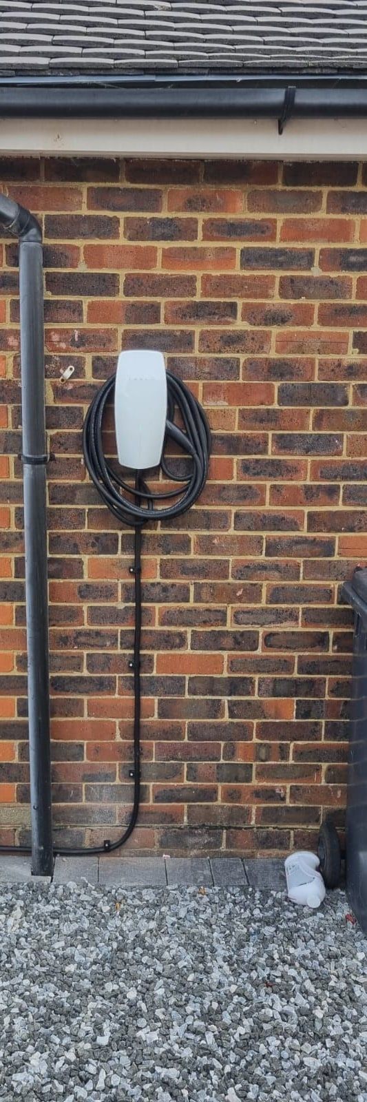 A tethered EV charger on a brick wall beside a gravel drive
