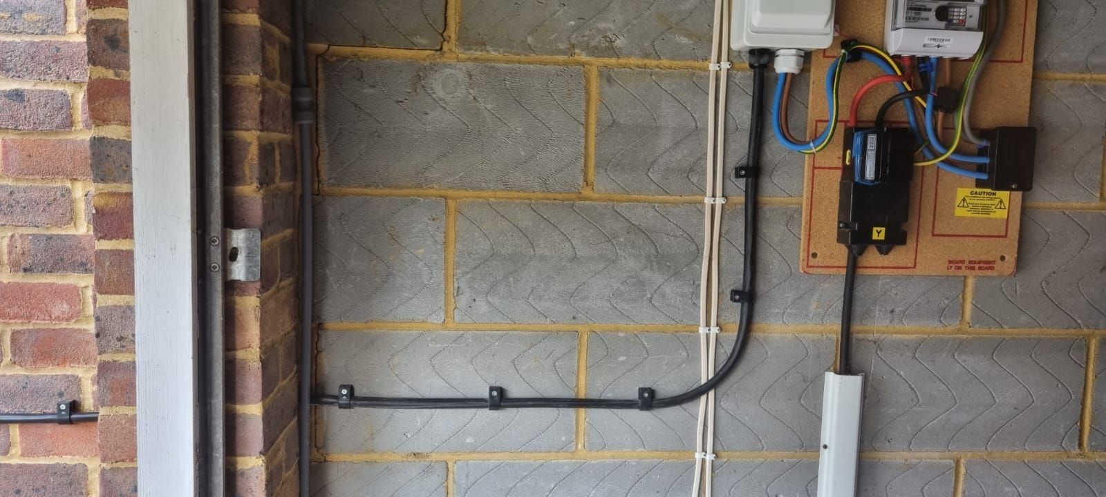 The supply side of a charger installation: meter tails, an isolator and a clipped cable run on a garage wall