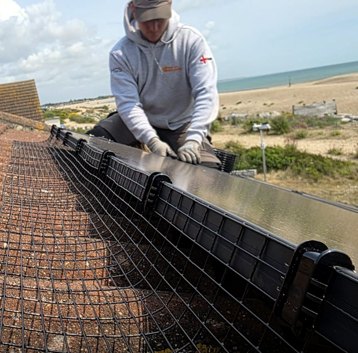 An installer fitting bird mesh along a solar array with the sea in the distance