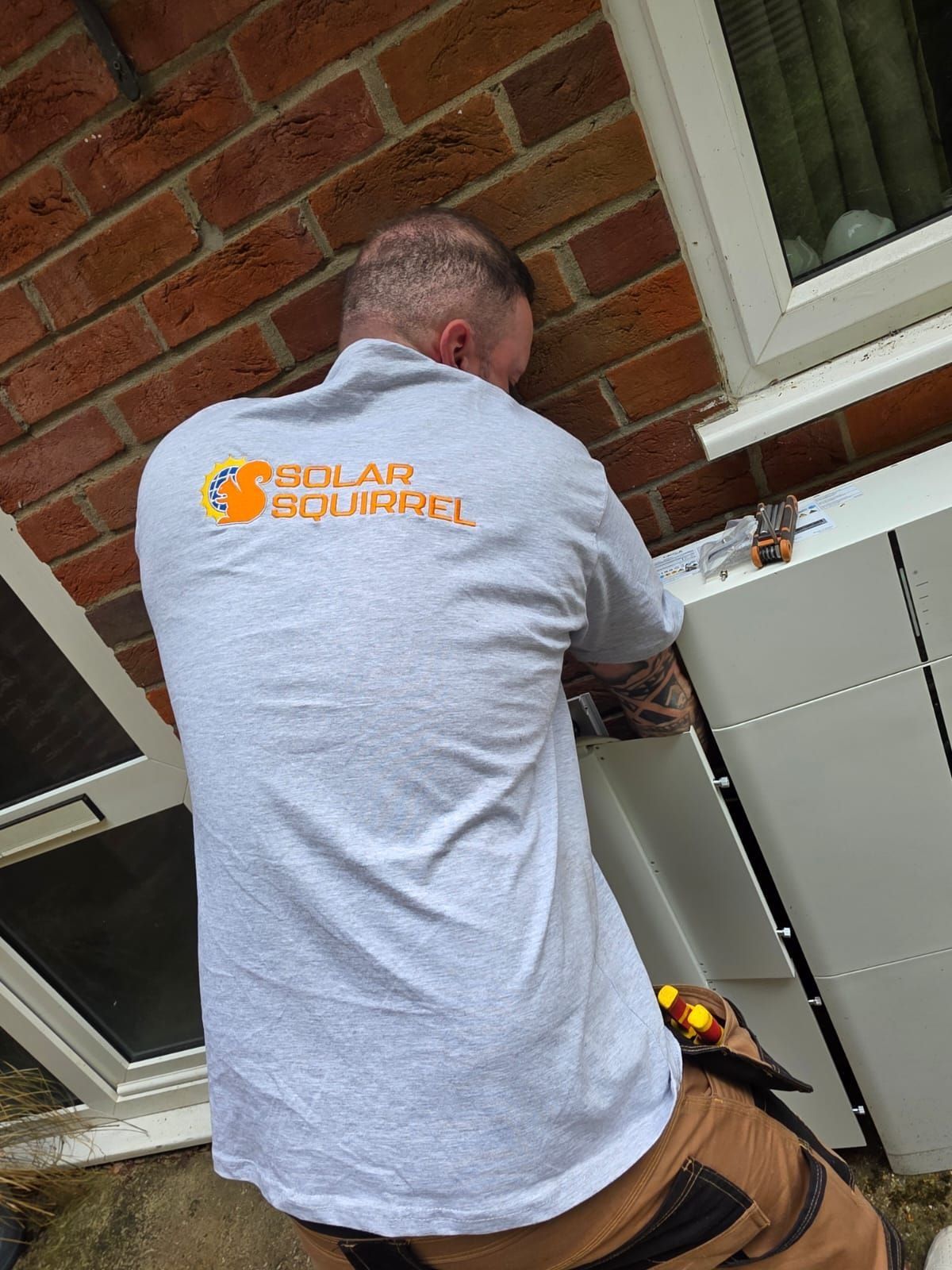 A Solar Squirrel installer fitting a battery stack against an outside wall