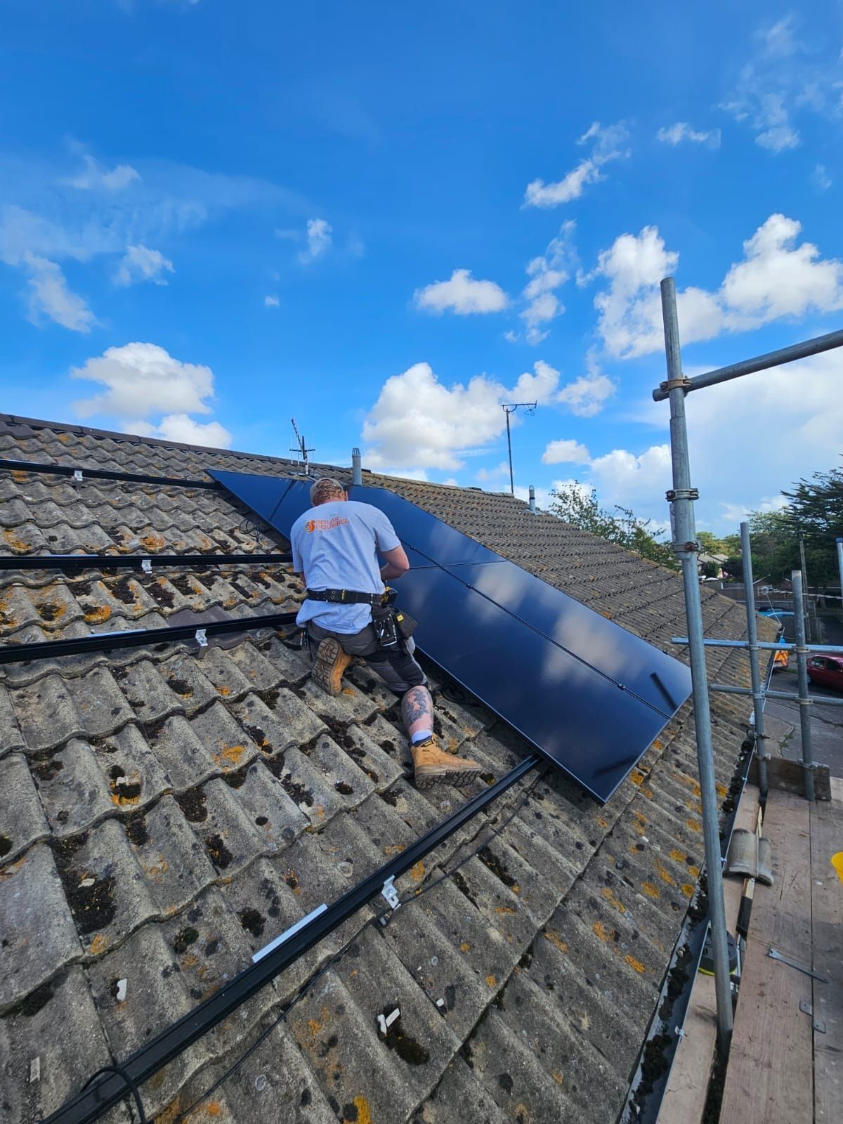 A Solar Squirrel installer placing all-black panels on a tiled roof, scaffold edge protection alongside
